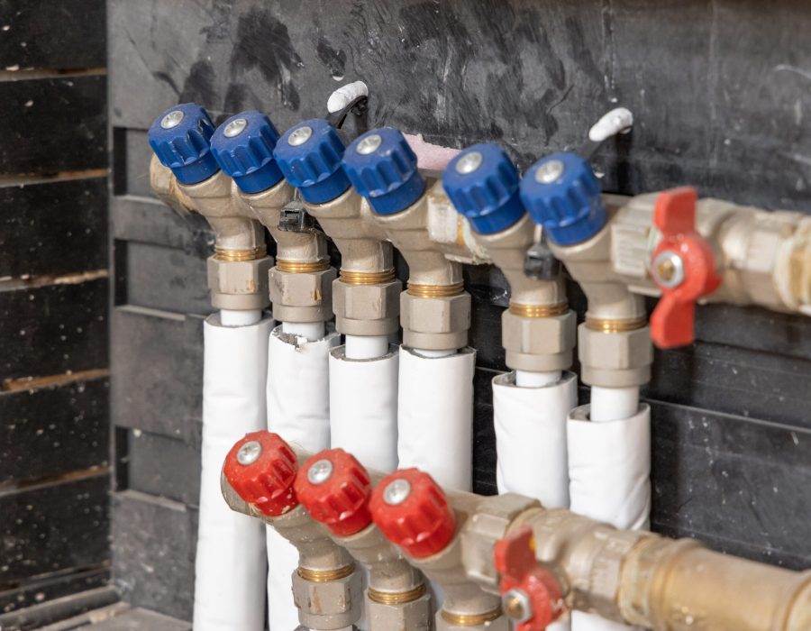 A collector with pipes and valves for hot and cold water in heating and water supply system closeup. Closeup of domestic boiler room for house heating and watering. Underfloor heating system
