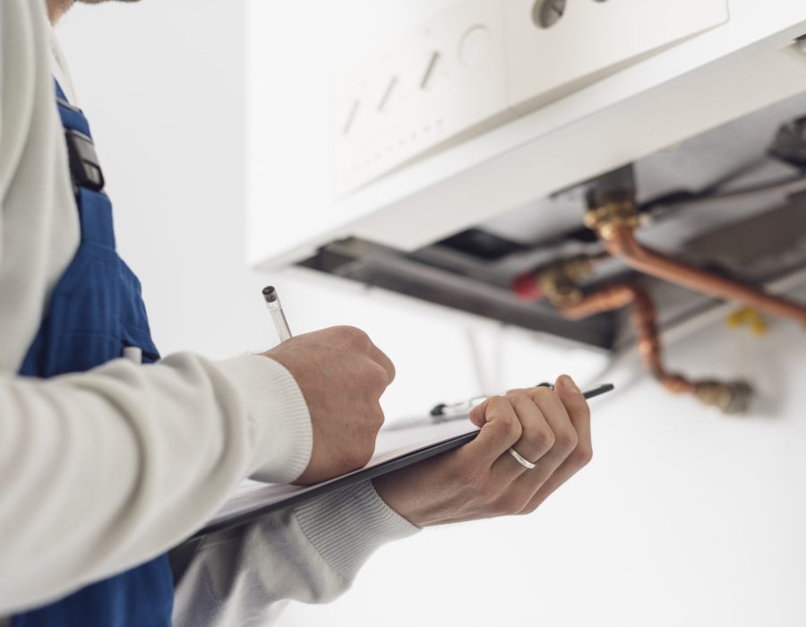 Professional plumber checking a boiler at home and writing on a clipboard