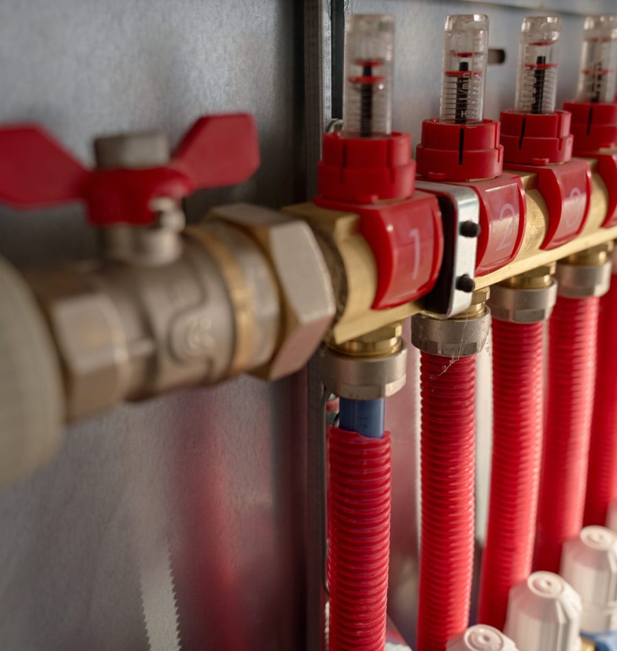 Underfloor heating manifold with control valves, flow meters and connected red pipes. Home heating system, plumbing and temperature control concept
